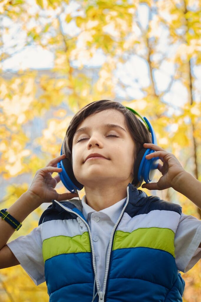 A young boy enjoys music through headphones amidst colorful fall foliage.