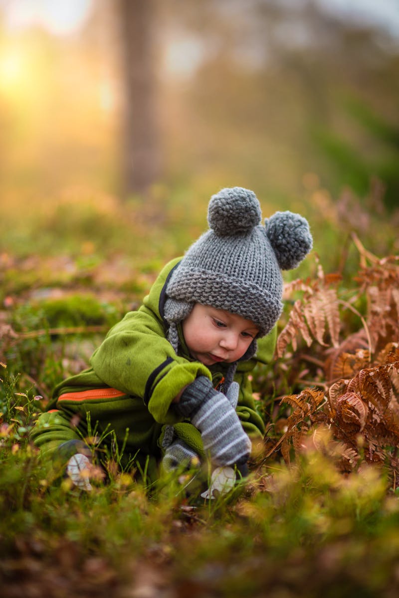 A cute baby in a knit hat and green outfit exploring nature during sunset.