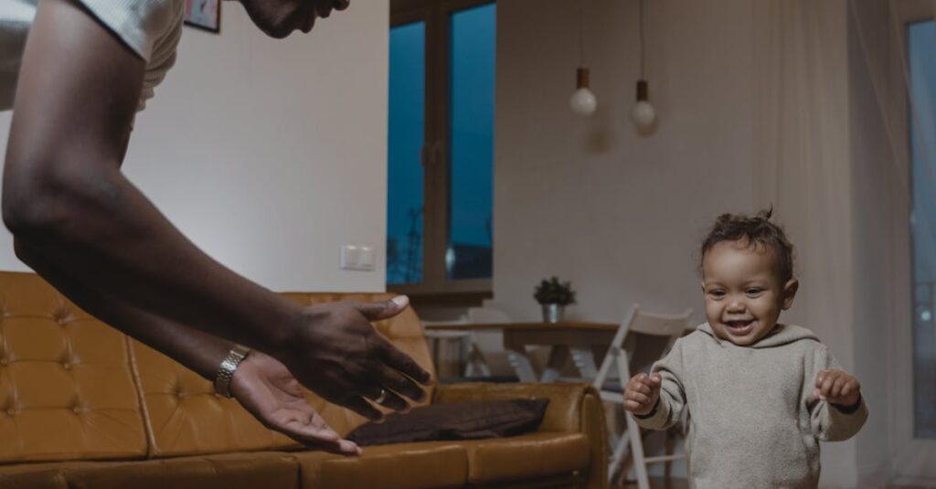 A joyful father watches his baby take first steps in a cozy living room setting.